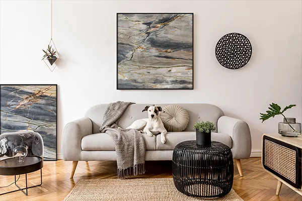 Foto eines STEINBILDS (Gemälde aus Naturstein, umrahmt von einem hochwertigen, schwarzen Holzrahmen), aufgehangen in einem Wohnzimmer. Zu sehen ist außerdem noch ein Hund auf einer Couch unter dem STEINBILD. Zusätzlich steht ein STEINBILD links neben der Couch auf dem Boden.